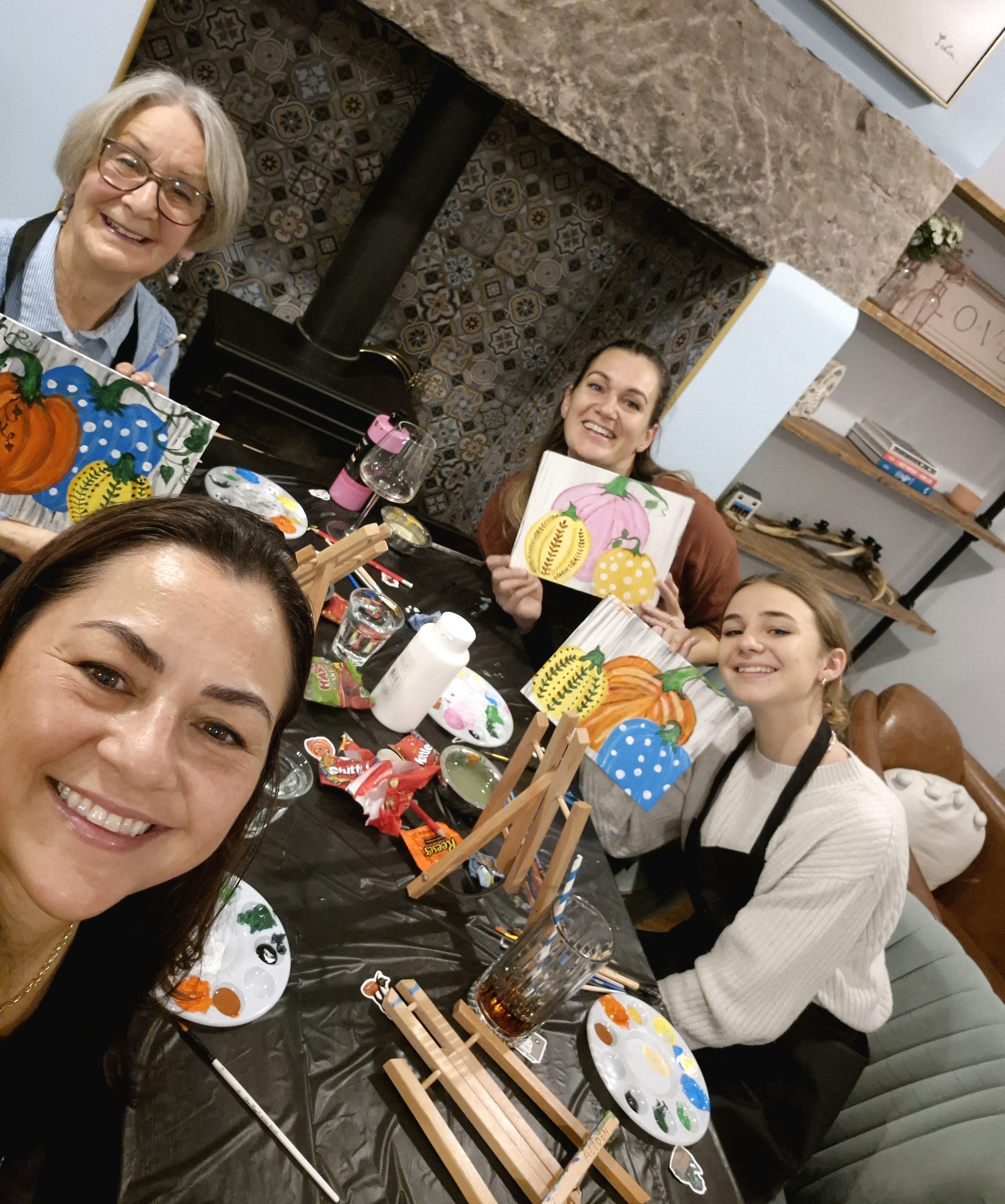 Photo of 3 people holding their completed paintings at the end of a Paint and Sip event.