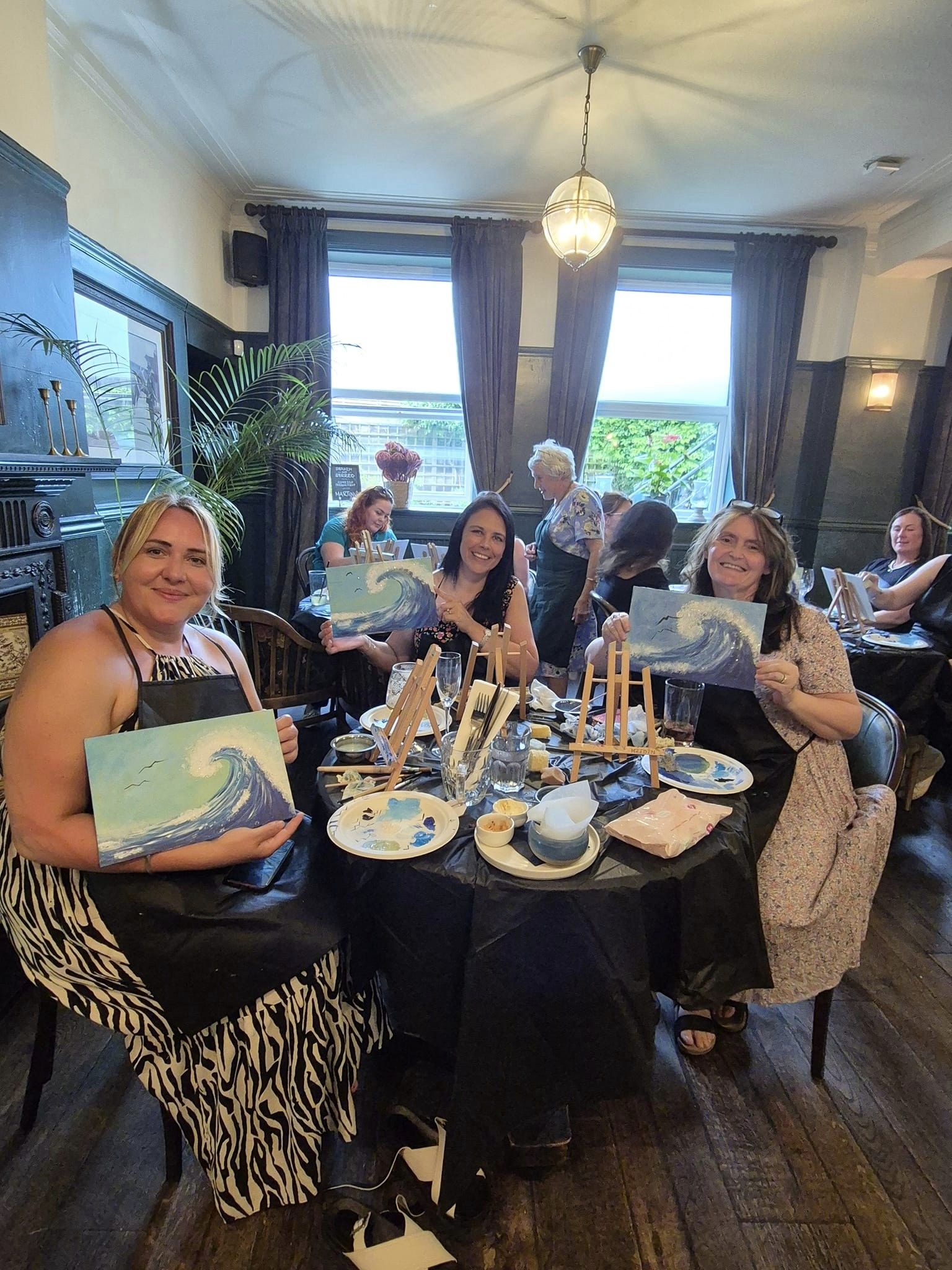 Picture of 3 people holding their completed paintings at the end of a Paint and Sip event.